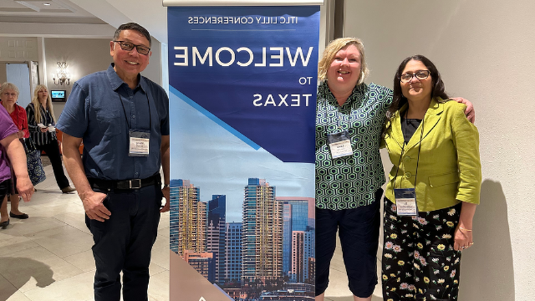 Three people smile in front of a banner